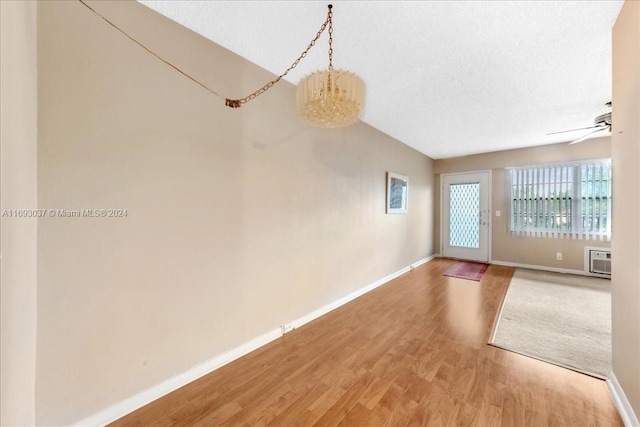 unfurnished living room featuring an AC wall unit, ceiling fan with notable chandelier, wood-type flooring, and a textured ceiling