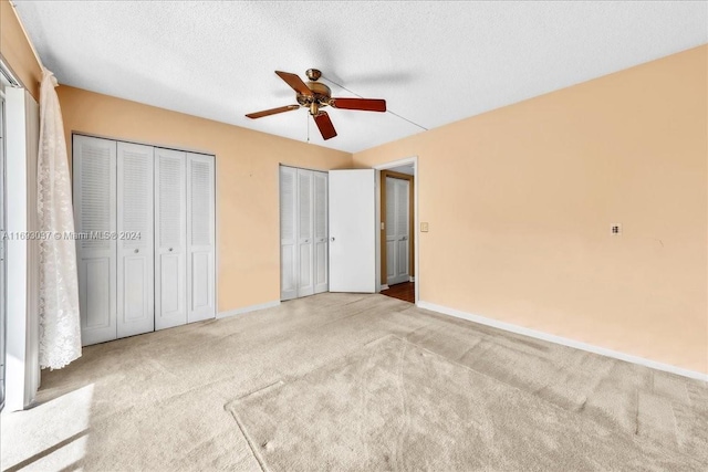 unfurnished bedroom with light carpet, a textured ceiling, ceiling fan, and multiple closets