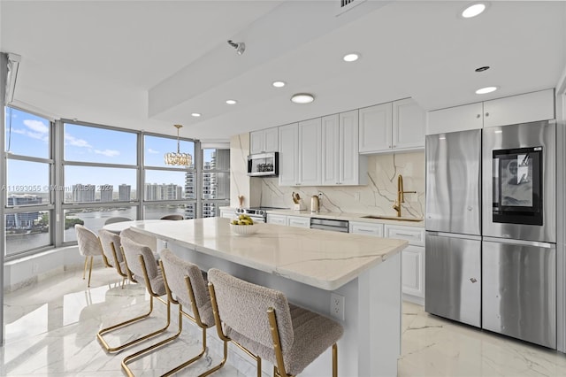 kitchen with hanging light fixtures, appliances with stainless steel finishes, white cabinetry, and a wealth of natural light