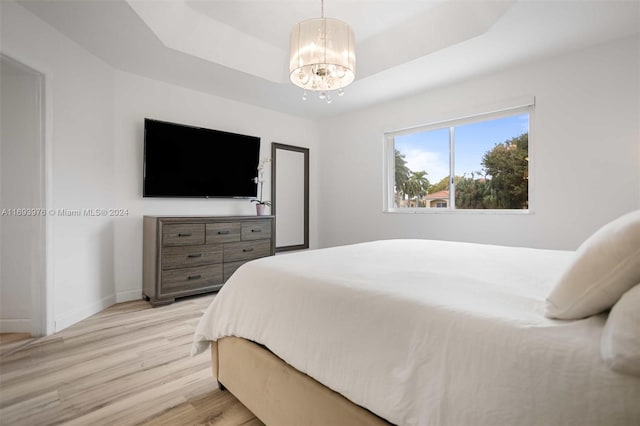 bedroom with a raised ceiling, light hardwood / wood-style flooring, and a notable chandelier