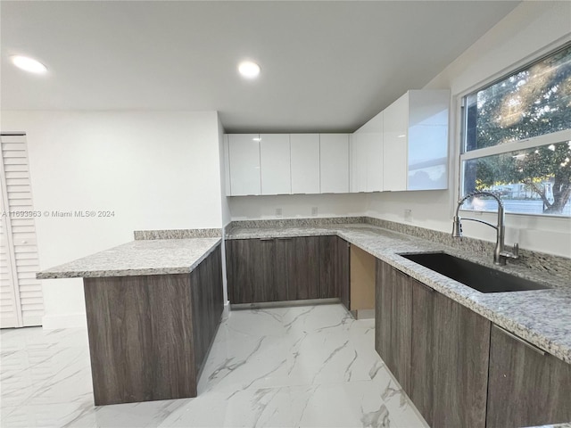 kitchen featuring white cabinets, light stone countertops, and sink