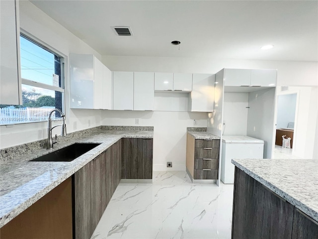 kitchen featuring white cabinetry, sink, fridge, dark brown cabinetry, and light stone countertops