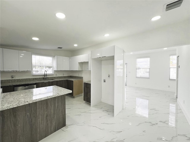 kitchen with sink, white cabinetry, a center island, dark brown cabinetry, and light stone countertops