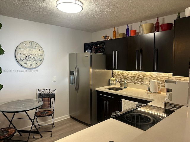 kitchen featuring backsplash, sink, stainless steel fridge, a textured ceiling, and light hardwood / wood-style floors