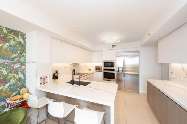 kitchen with kitchen peninsula, built in appliances, white cabinetry, and sink