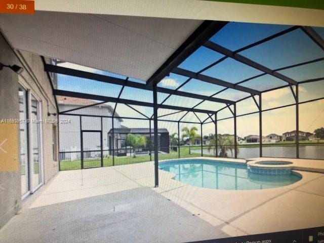 view of pool with a patio area, a water view, glass enclosure, and an in ground hot tub