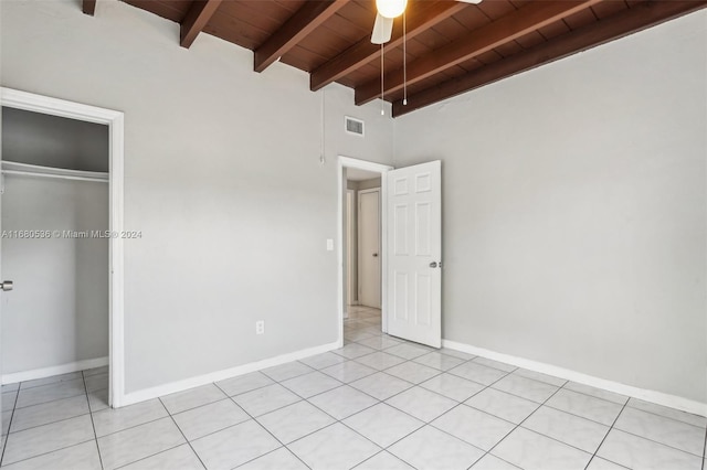 unfurnished bedroom with ceiling fan, light tile patterned floors, beam ceiling, wood ceiling, and a closet