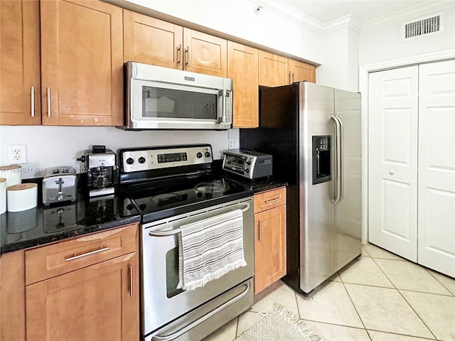 kitchen featuring light tile patterned floors, dark stone countertops, ornamental molding, and appliances with stainless steel finishes