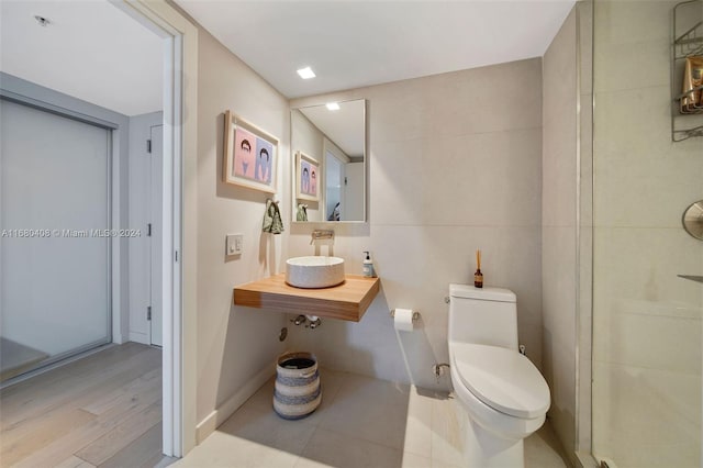 bathroom featuring sink, wood-type flooring, an enclosed shower, toilet, and tile walls