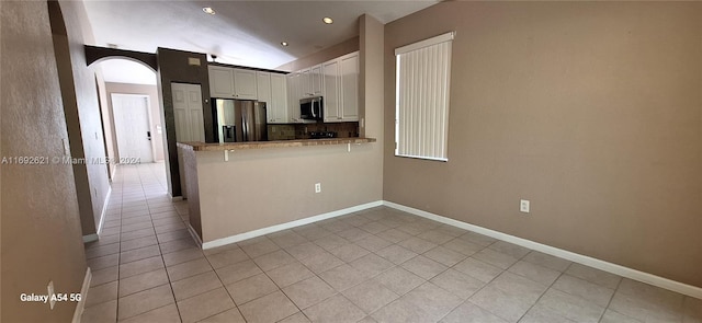 kitchen featuring white cabinetry, kitchen peninsula, vaulted ceiling, light tile patterned floors, and appliances with stainless steel finishes