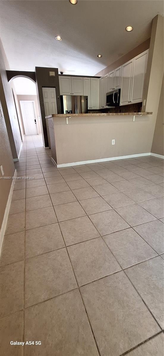 kitchen with kitchen peninsula, white cabinetry, light tile patterned floors, and stainless steel appliances