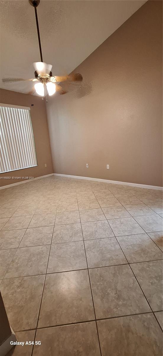 empty room with ceiling fan, light tile patterned floors, and lofted ceiling