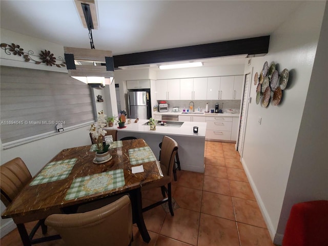 dining space with light tile patterned flooring, beam ceiling, and sink