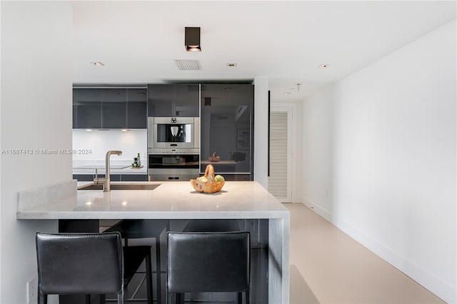 kitchen with sink, stainless steel double oven, light stone counters, kitchen peninsula, and a breakfast bar