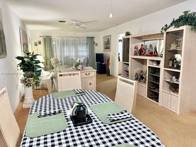 dining area with ceiling fan, light colored carpet, and a textured ceiling