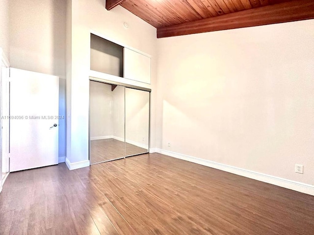 unfurnished bedroom featuring beam ceiling, a closet, wood ceiling, and hardwood / wood-style flooring