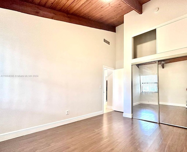 unfurnished bedroom featuring a closet, beamed ceiling, wooden ceiling, and hardwood / wood-style flooring