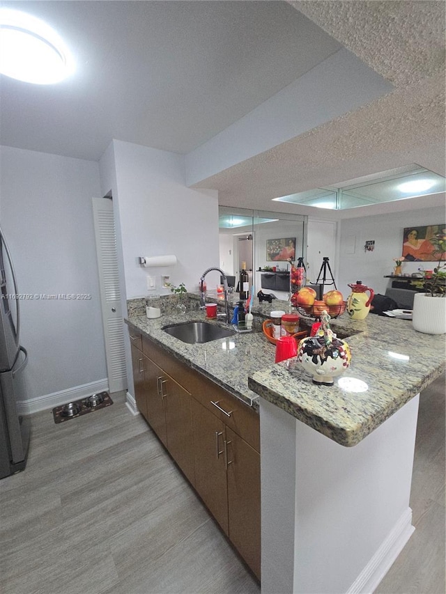 kitchen featuring dark brown cabinets, sink, light wood-type flooring, and kitchen peninsula