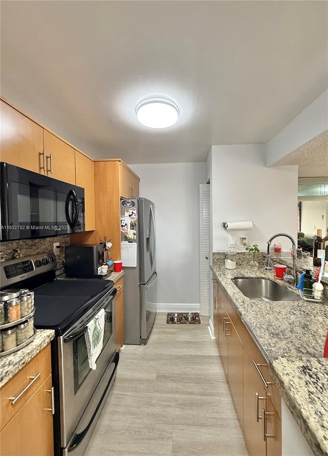 kitchen featuring light stone counters, sink, light hardwood / wood-style floors, and appliances with stainless steel finishes