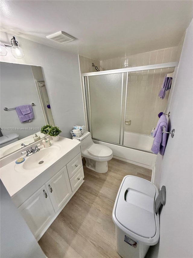 full bathroom with hardwood / wood-style flooring, enclosed tub / shower combo, vanity, and toilet