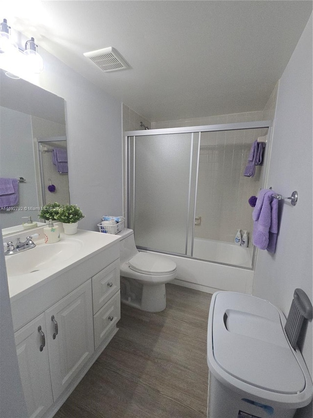 full bathroom with hardwood / wood-style flooring, bath / shower combo with glass door, vanity, and toilet