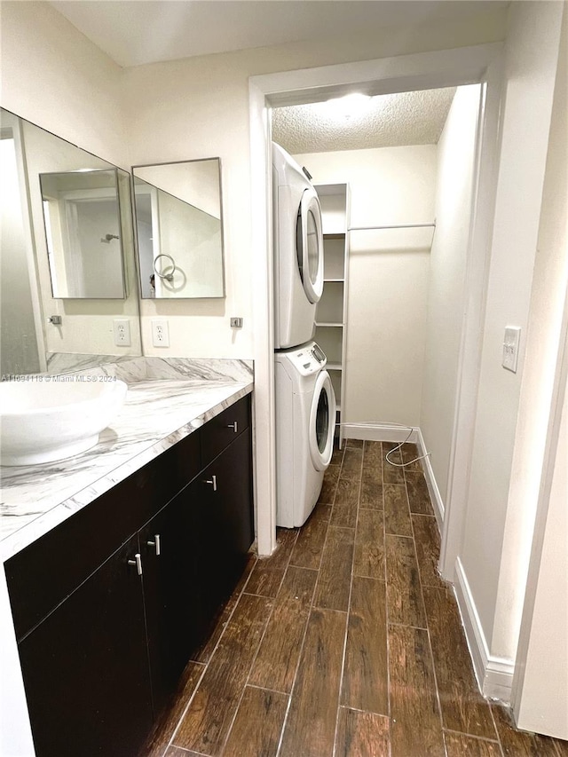 laundry room with a textured ceiling, stacked washer and dryer, dark hardwood / wood-style floors, and sink