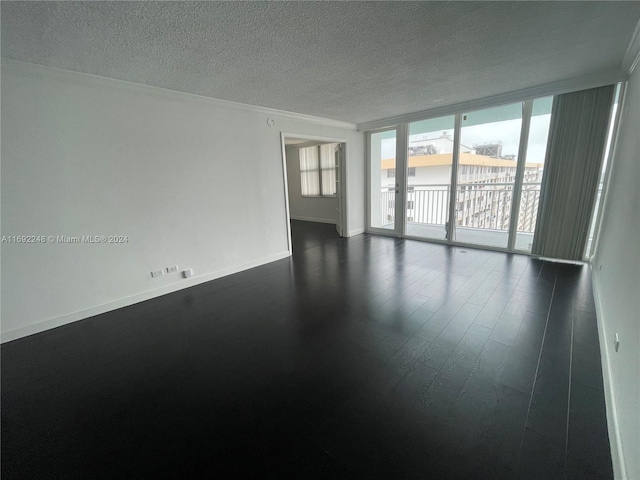 empty room featuring a textured ceiling, expansive windows, ornamental molding, and dark wood-type flooring