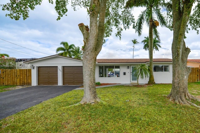 ranch-style home with driveway, stucco siding, fence, an attached garage, and a front lawn