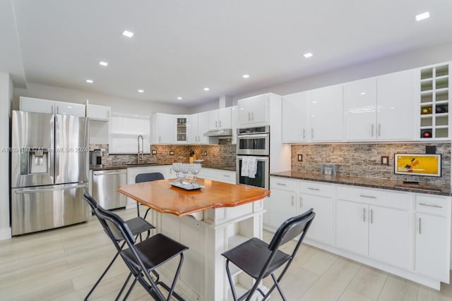 kitchen with under cabinet range hood, white cabinets, stainless steel appliances, and glass insert cabinets