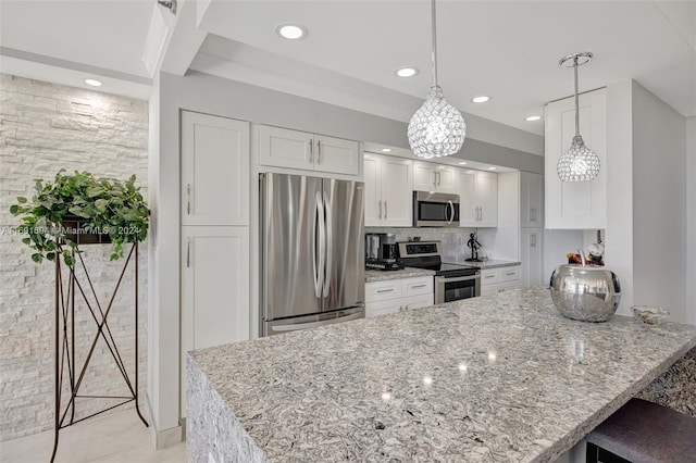 kitchen with light stone countertops, appliances with stainless steel finishes, backsplash, white cabinetry, and hanging light fixtures