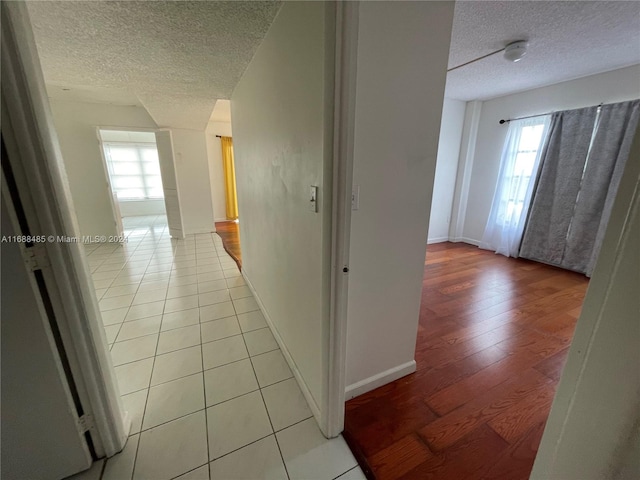 hall with a textured ceiling, light wood-type flooring, and a wealth of natural light