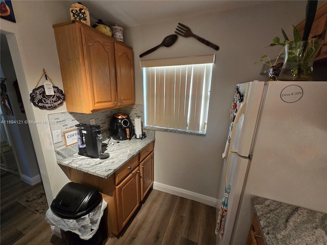 kitchen with dark hardwood / wood-style flooring, backsplash, white fridge, and light stone counters