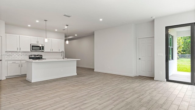 kitchen with a kitchen island with sink, white cabinets, stainless steel appliances, and decorative light fixtures