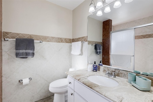 bathroom with vanity, toilet, a shower with shower door, and tile walls