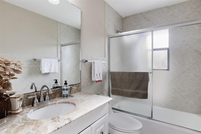 full bathroom featuring vanity, toilet, enclosed tub / shower combo, and tile walls