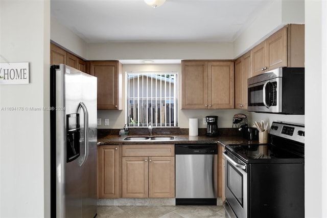 kitchen featuring sink, light tile patterned floors, dark stone counters, and appliances with stainless steel finishes