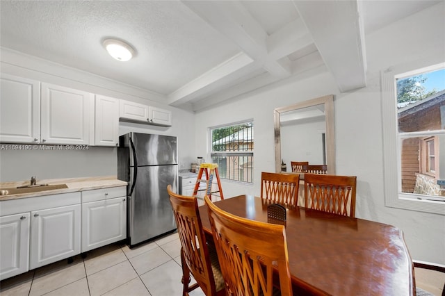 kitchen with a wealth of natural light, stainless steel fridge, beamed ceiling, and white cabinets