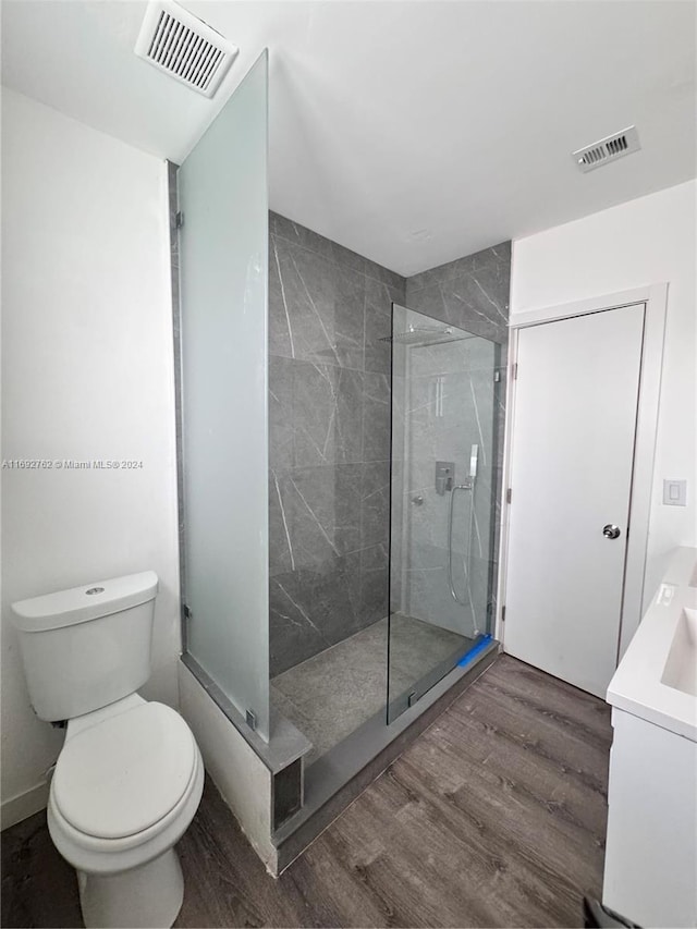 bathroom featuring a tile shower, toilet, vanity, and hardwood / wood-style flooring