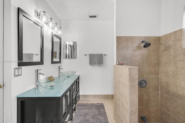 full bathroom featuring tile patterned flooring, double vanity, a tile shower, and a sink
