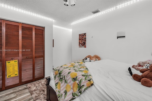 bedroom with light wood-style flooring, visible vents, a closet, and a textured ceiling