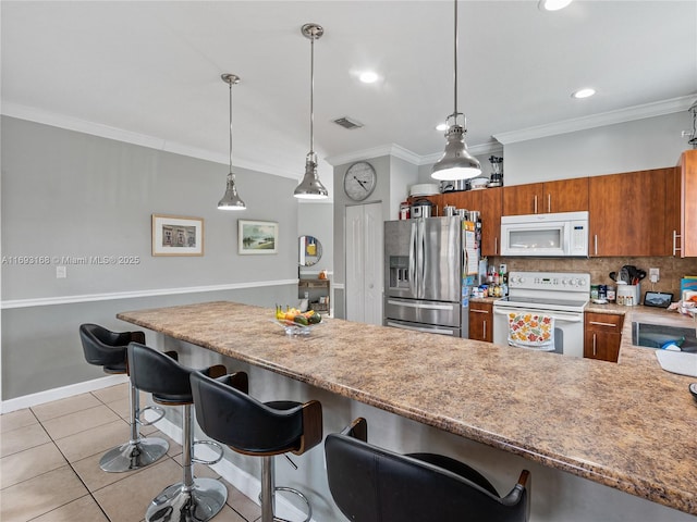 kitchen with light tile patterned floors, white appliances, crown molding, and a kitchen breakfast bar