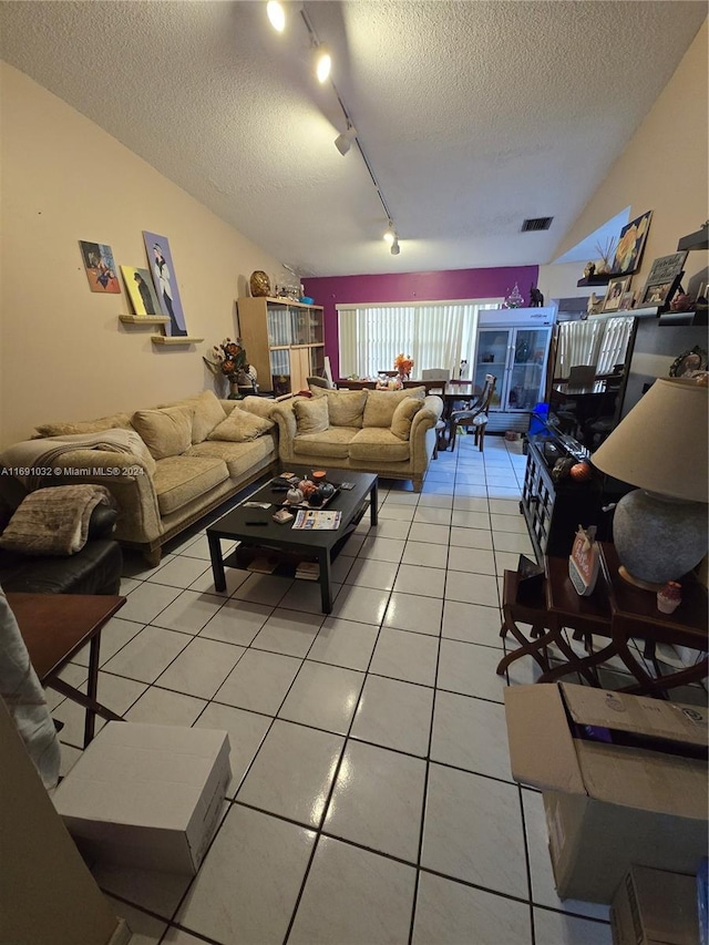 living room featuring a textured ceiling, rail lighting, vaulted ceiling, and tile patterned floors