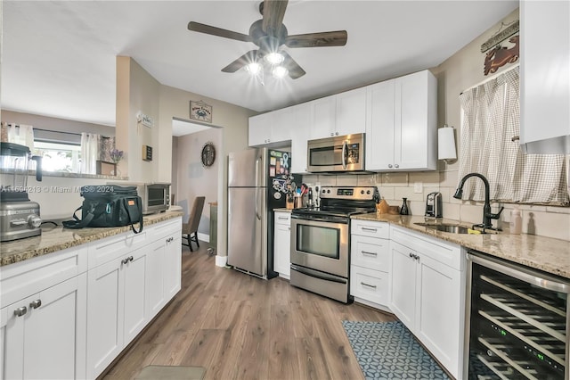 kitchen with appliances with stainless steel finishes, light stone counters, beverage cooler, sink, and white cabinets