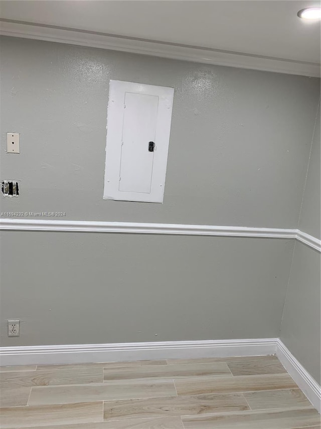 spare room with wood-type flooring, crown molding, and electric panel