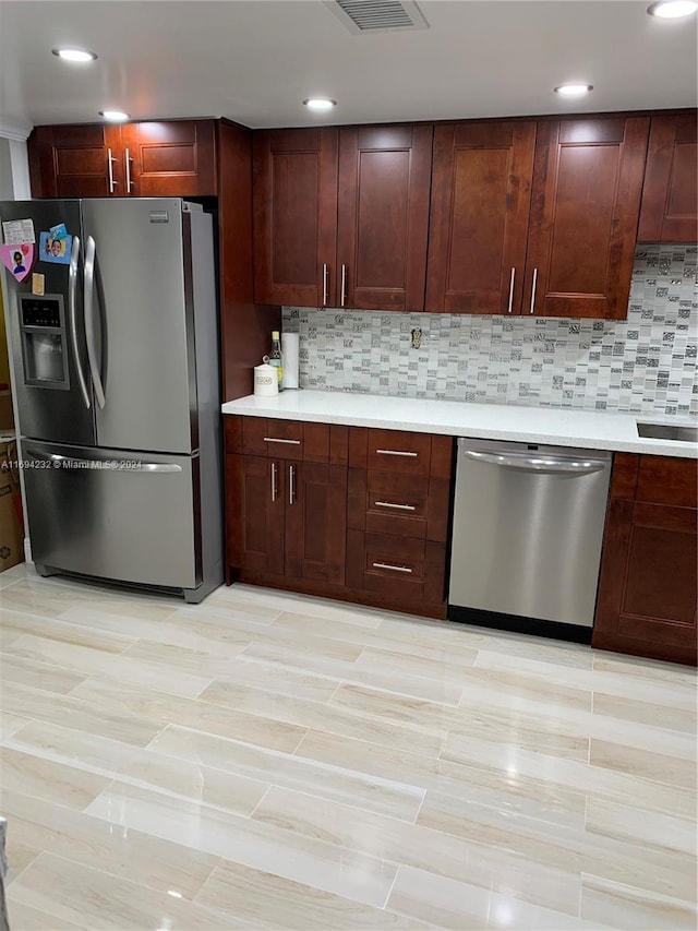 kitchen with appliances with stainless steel finishes, backsplash, and light hardwood / wood-style flooring