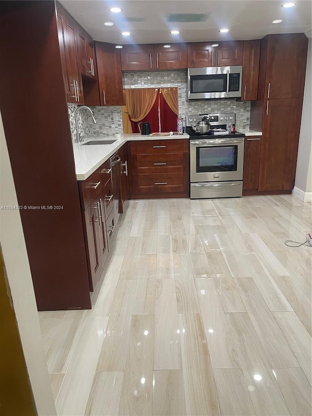 kitchen with appliances with stainless steel finishes, light wood-type flooring, tasteful backsplash, and sink