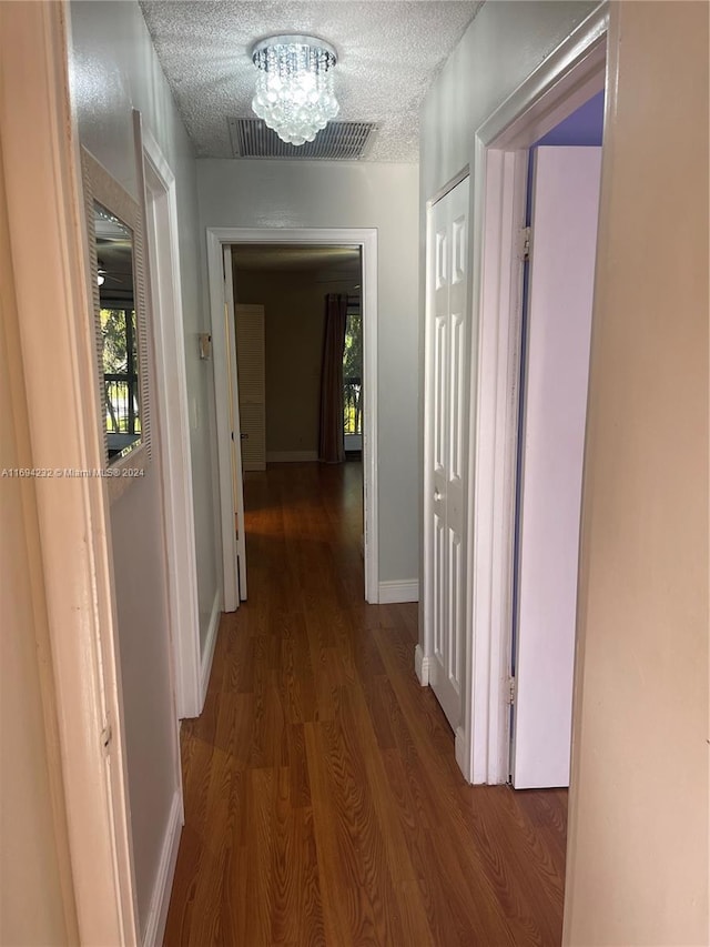 corridor featuring hardwood / wood-style flooring, a textured ceiling, and a chandelier