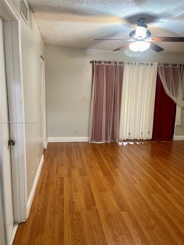 unfurnished room with ceiling fan, wood-type flooring, and a textured ceiling