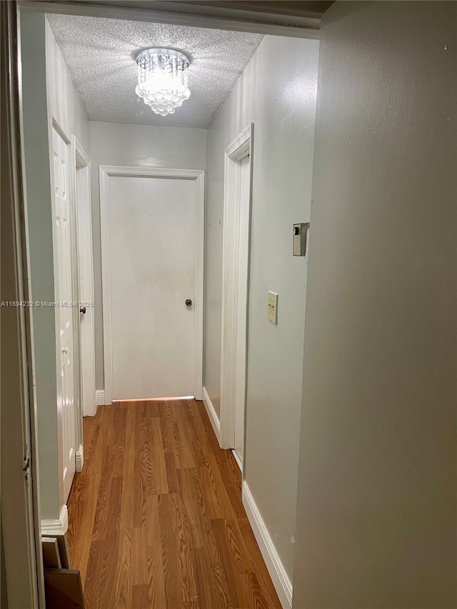 hallway with a textured ceiling, baseboards, and wood finished floors