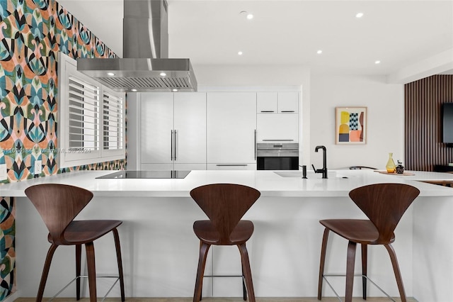 kitchen with kitchen peninsula, wall chimney exhaust hood, stainless steel oven, sink, and white cabinetry